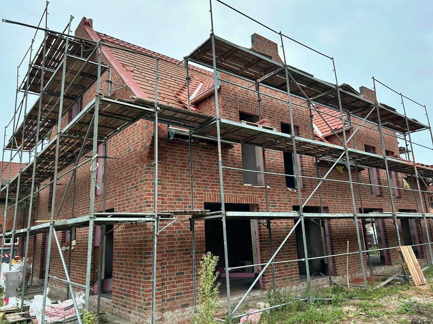 Rotbraunes Ziegelhaus mit rotem Dach hinter einem Baugerüst