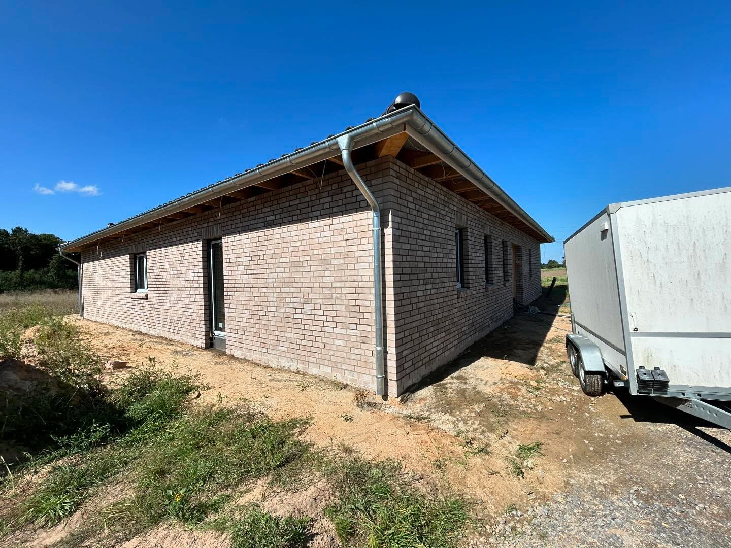 Grauer Klinkerbungalow mit Anhänger auf dem Grundstück