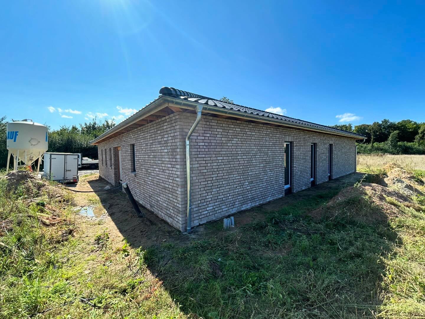 Grauer Klinkerbungalow mit hellem Metallwalmdach und Silo