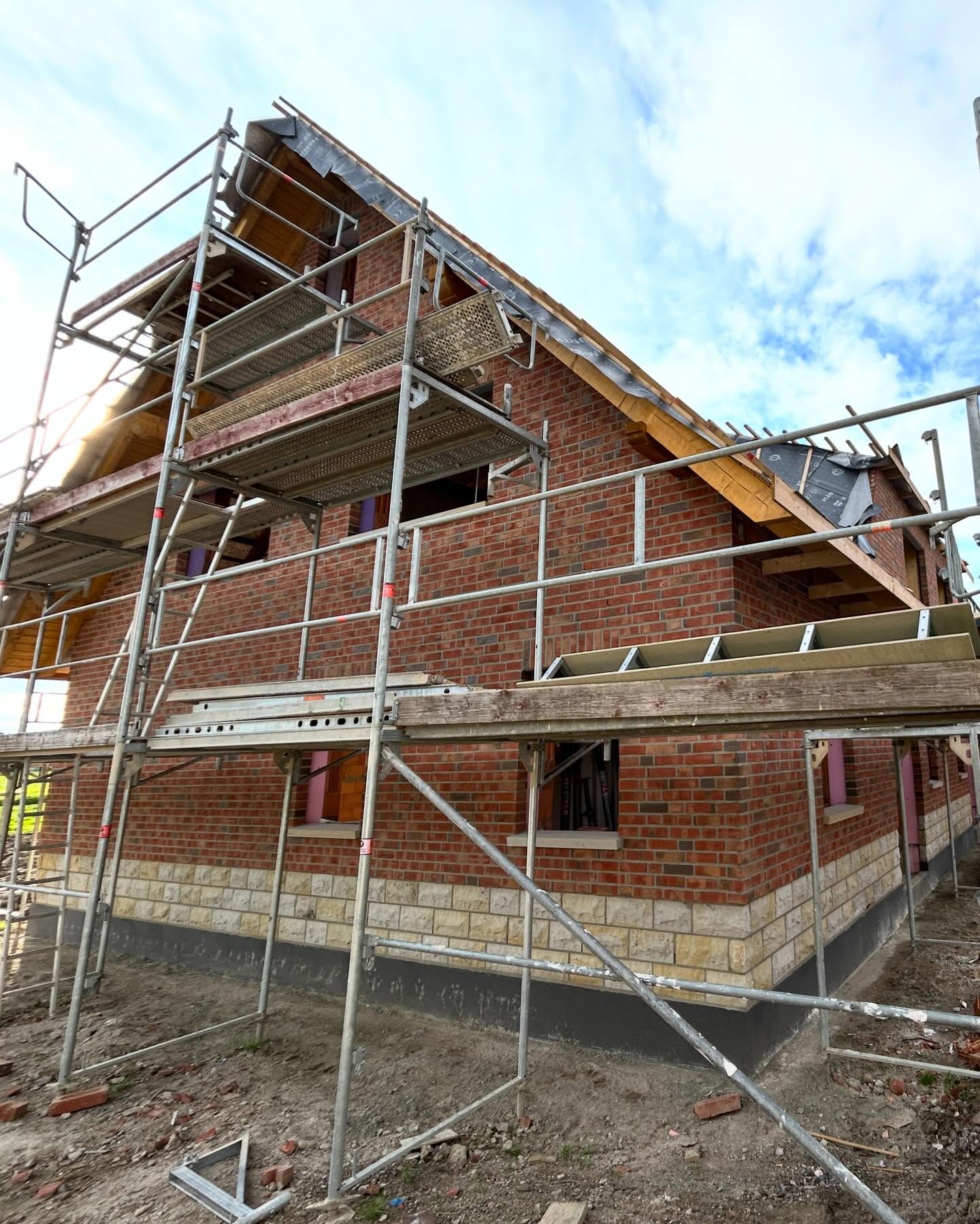 Giebelseite eines Hauses mit rotem Klinker, Natursteinsockel und Gerüst