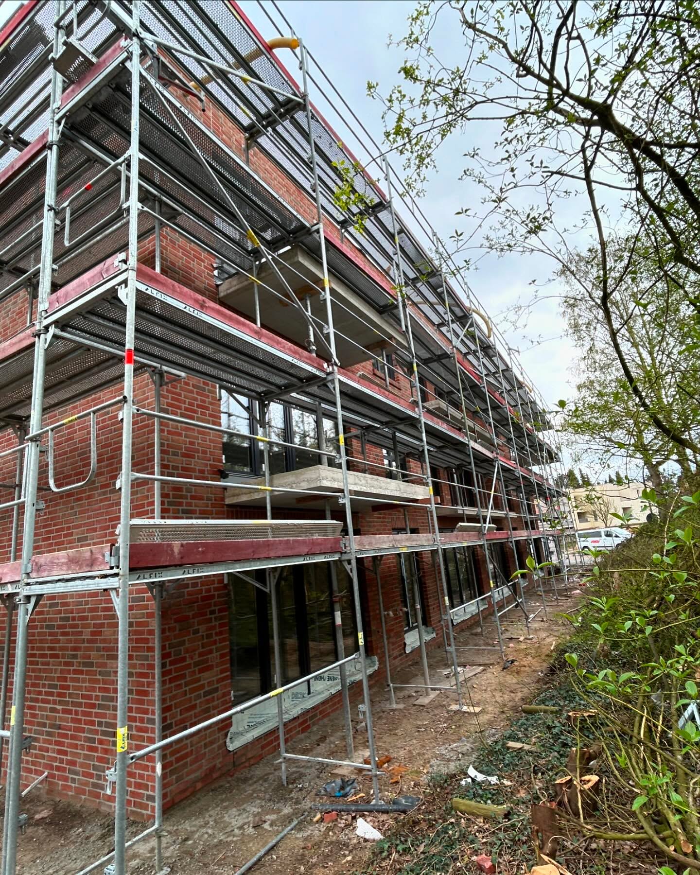 Rote Klinkerfassade hinter einem Baugerüst mit grünen Bäumen