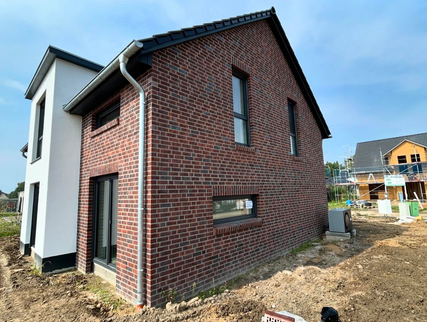 Rotes Klinkerhaus mit weißem Putzgiebel und schwarzen Fensterrahmen