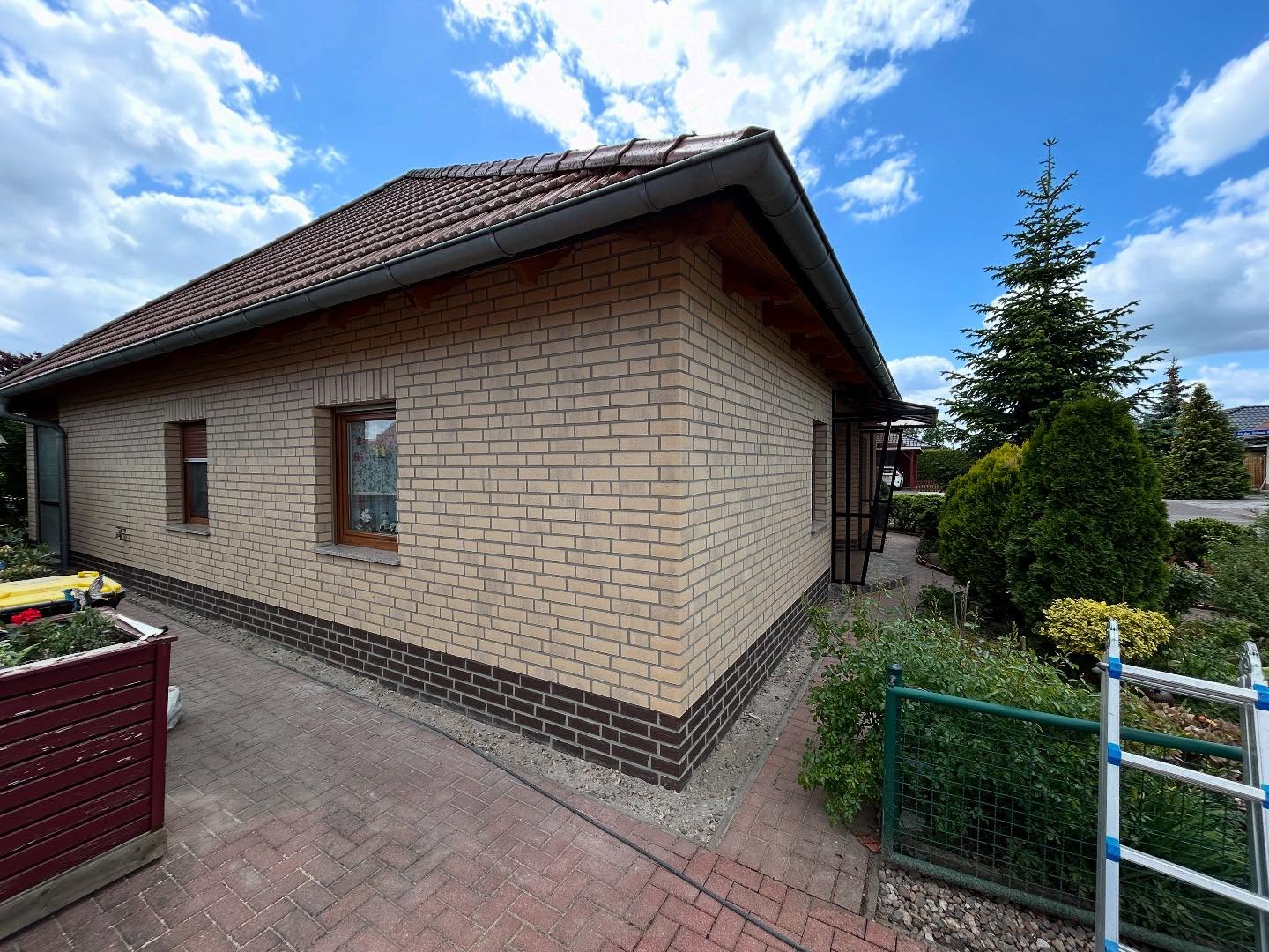 Heller Bungalow mit dunklem Sockel und Carport im Garten