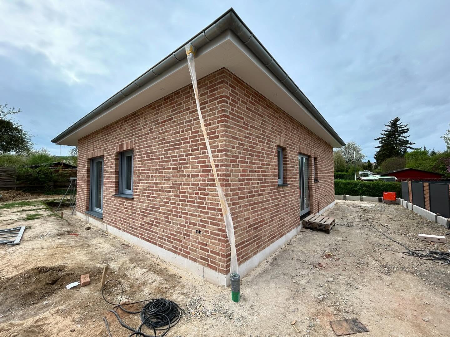 Roter Klinkerbungalow mit Fallrohr und umliegendem Garten