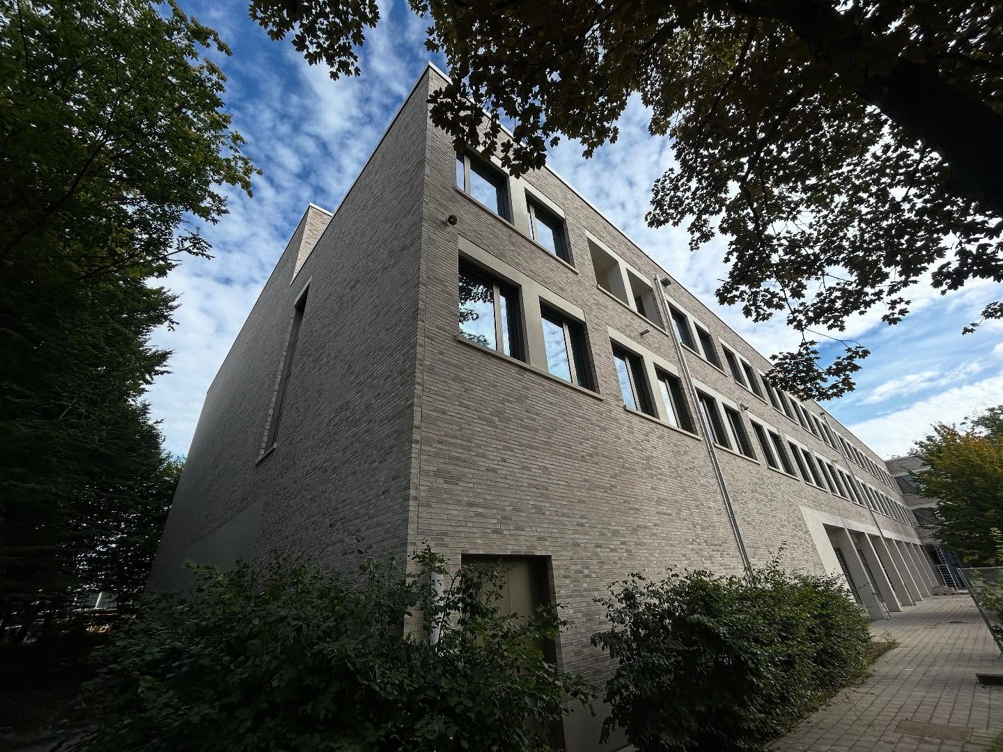 Großes helles Klinkergebäude an einer Straße mit Bäumen