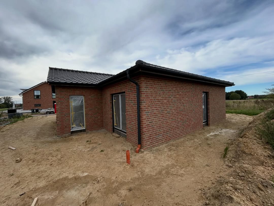 Roter Klinkerbungalow mit dunklem Walmdach auf dem Grundstück