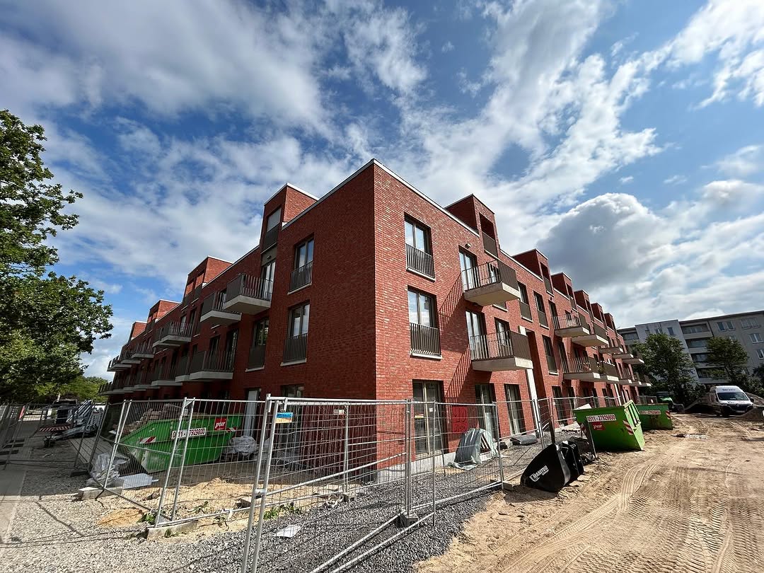 Mehrgeschossiges Wohngebäude mit roter Klinkerfassade und Bauzaun