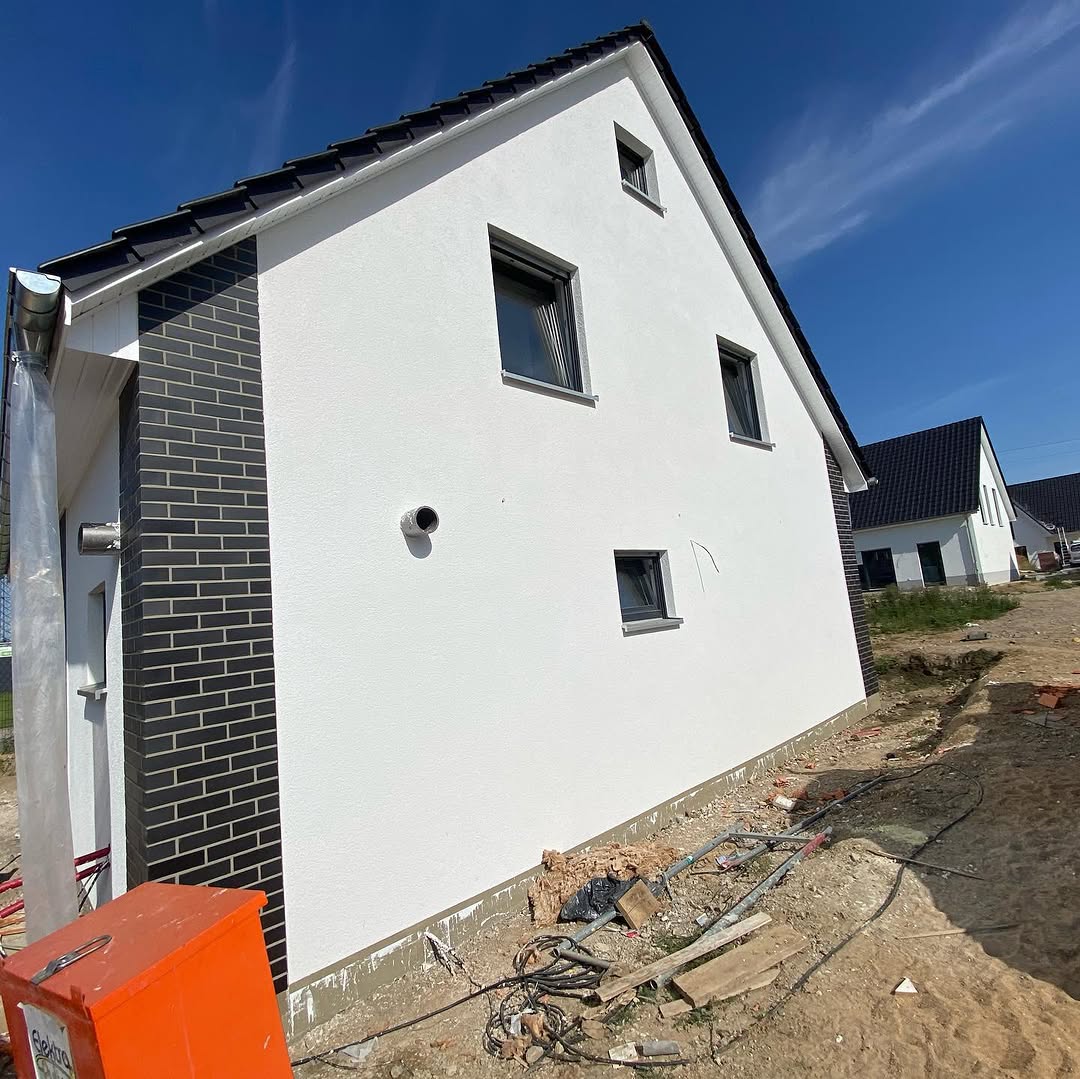 Weiße Putzfassade mit dunkler Klinkerfläche an einem Neubau