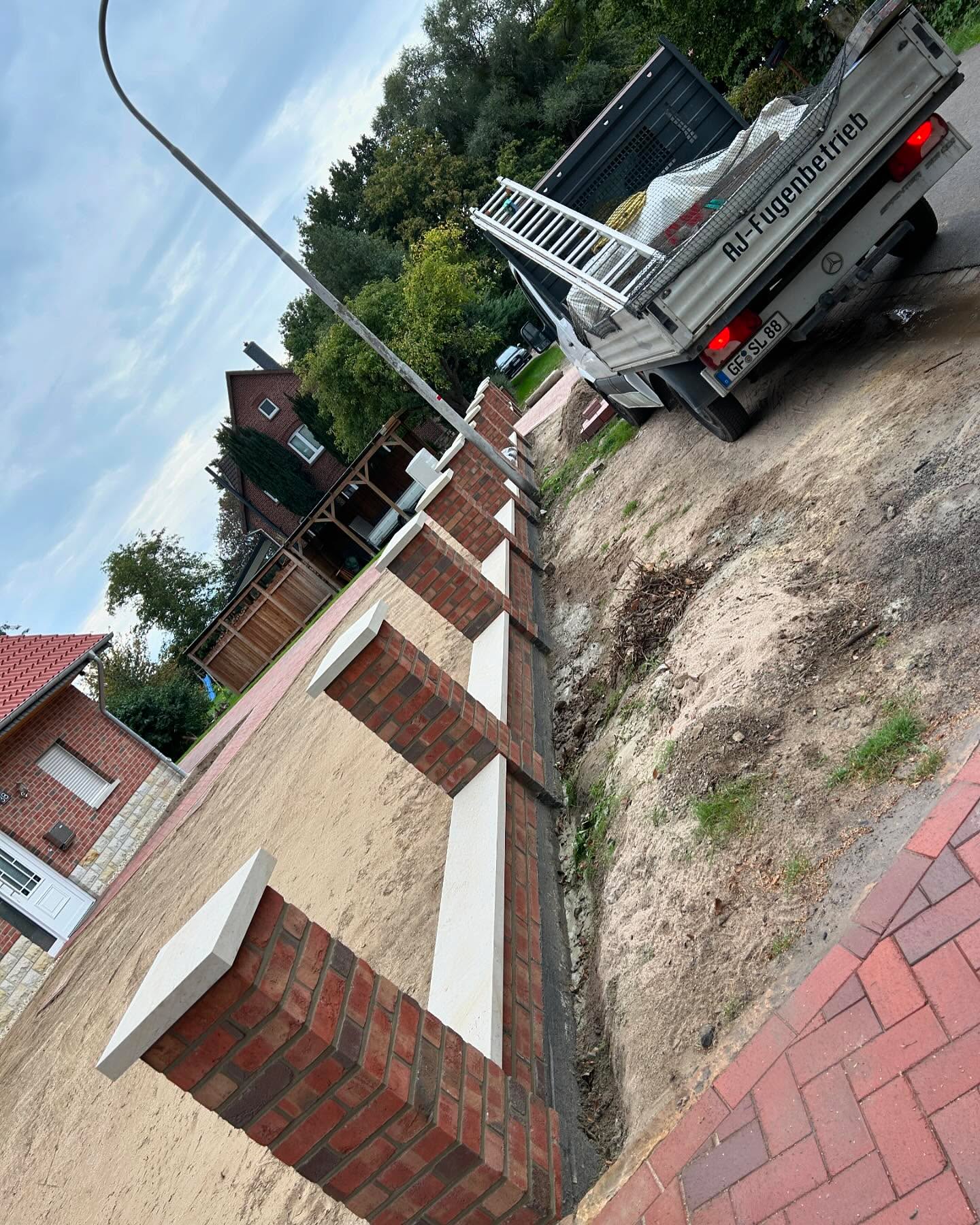 Rotbraune Klinkermauer mit weißen Pfeilerabdeckungen am Hang