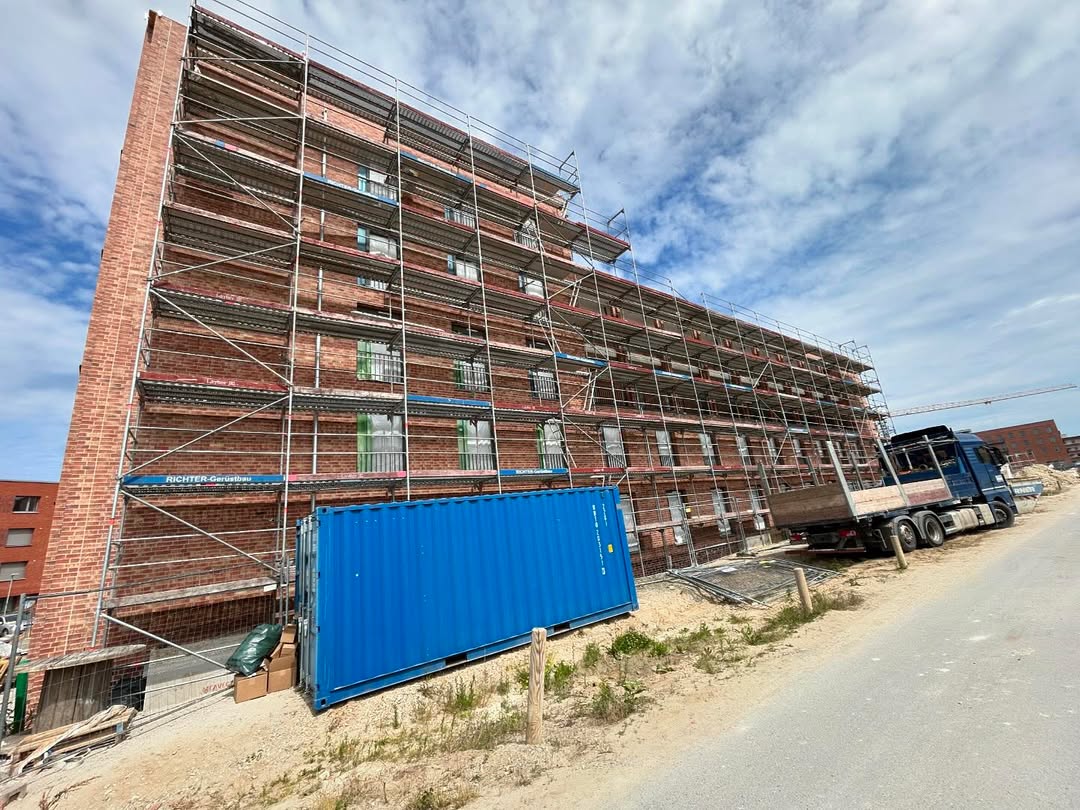 Hoch aufragendes Ziegelgebäude mit Gerüst und blauem Container