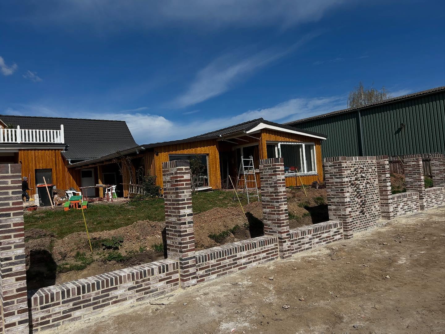 Neue Klinker-Gartenmauer vor einem Grundstück mit Holzhaus