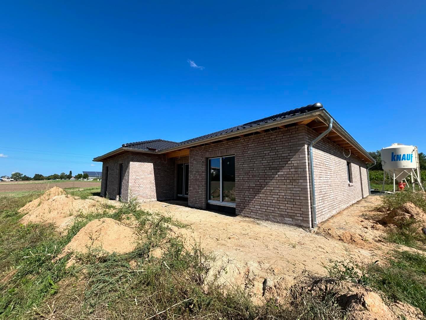 Grauer Klinkerbungalow auf einer Baustelle mit Silo