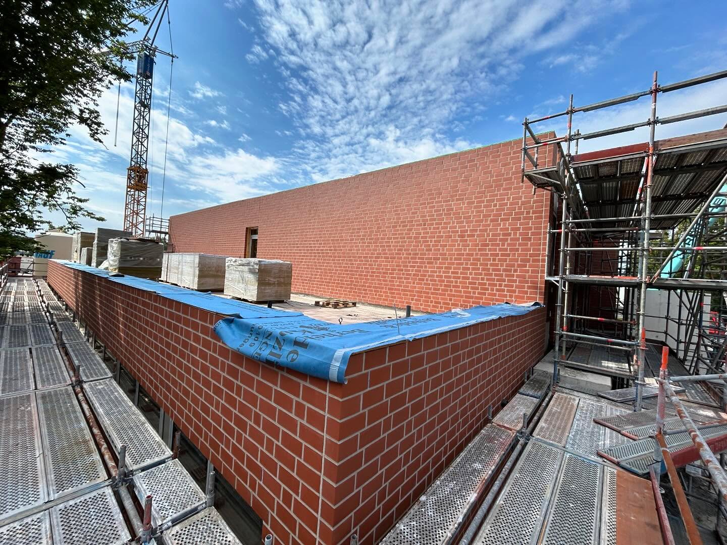 Lange rote Klinkerwand auf der Baustelle mit Kran und Gerüst
