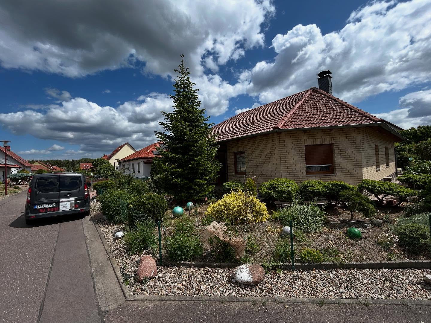 Fertiggestellter heller Bungalow mit gepflegtem Garten und Fahrzeug am Straßenrand