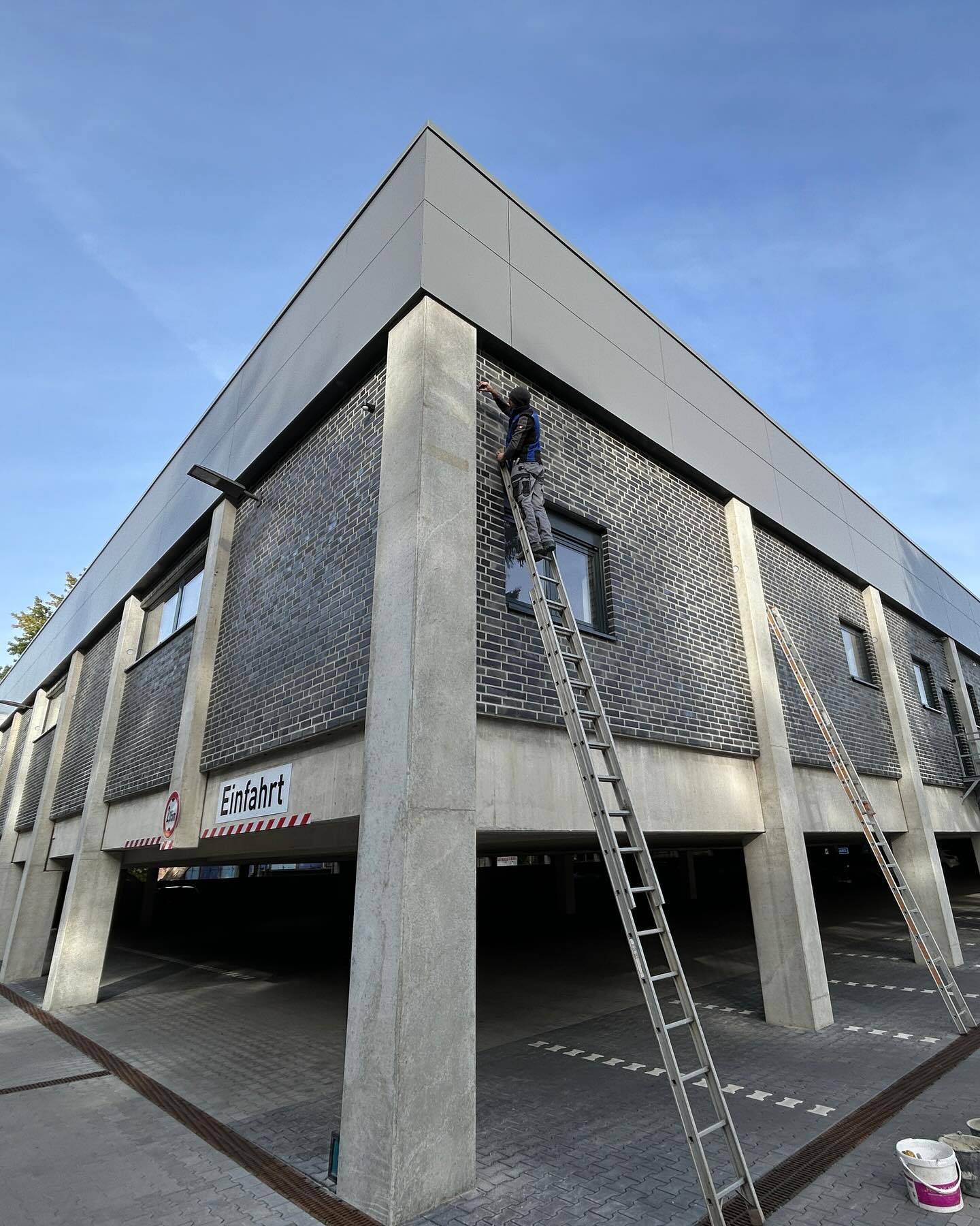 Dunkle Klinkerfassade mit Betonpfeilern über einer Tiefgarageneinfahrt