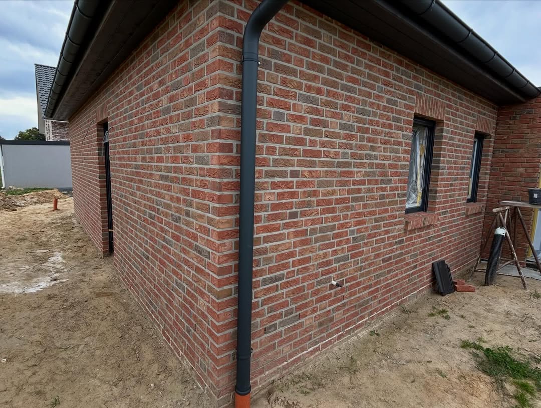 Rote Klinkerecke mit schwarzem Fallrohr und Fenster